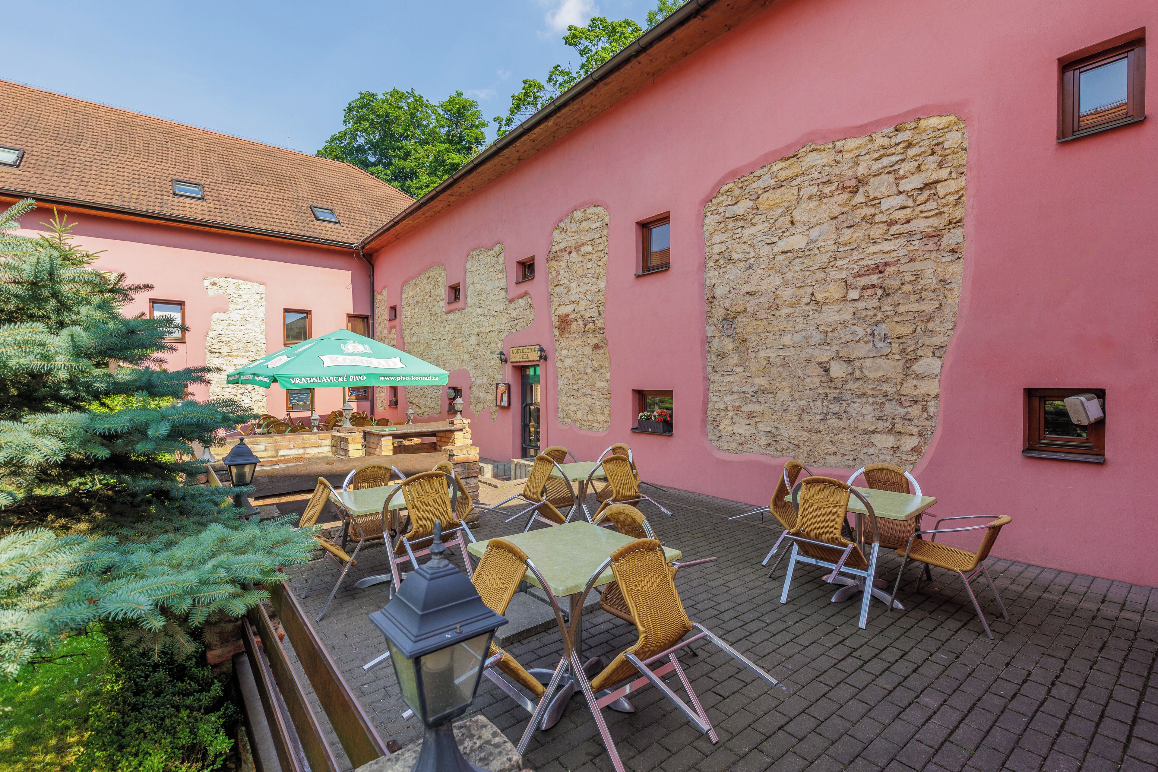 An outdoor seating area with wicker chairs and tables, a stone wall, and a green umbrella.