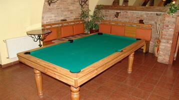 A pool table in a room with a brick wall, wooden benches, and a potted plant.
