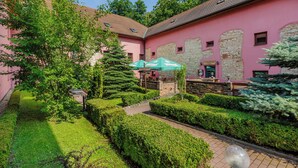 A pink building with stone walls, green trees, and a paved pathway. - Hotel Stary Pivovar (Prague)