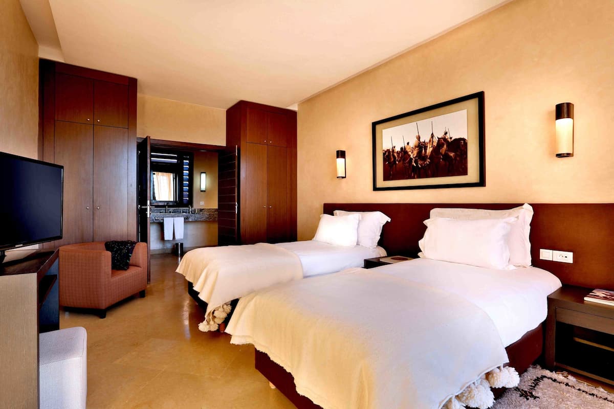 A hotel room with two beds, a TV, a sofa, and a painting on the wall.