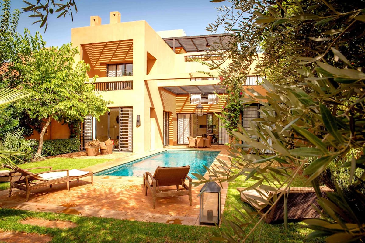 A modern house with a swimming pool, outdoor seating, and lush greenery.