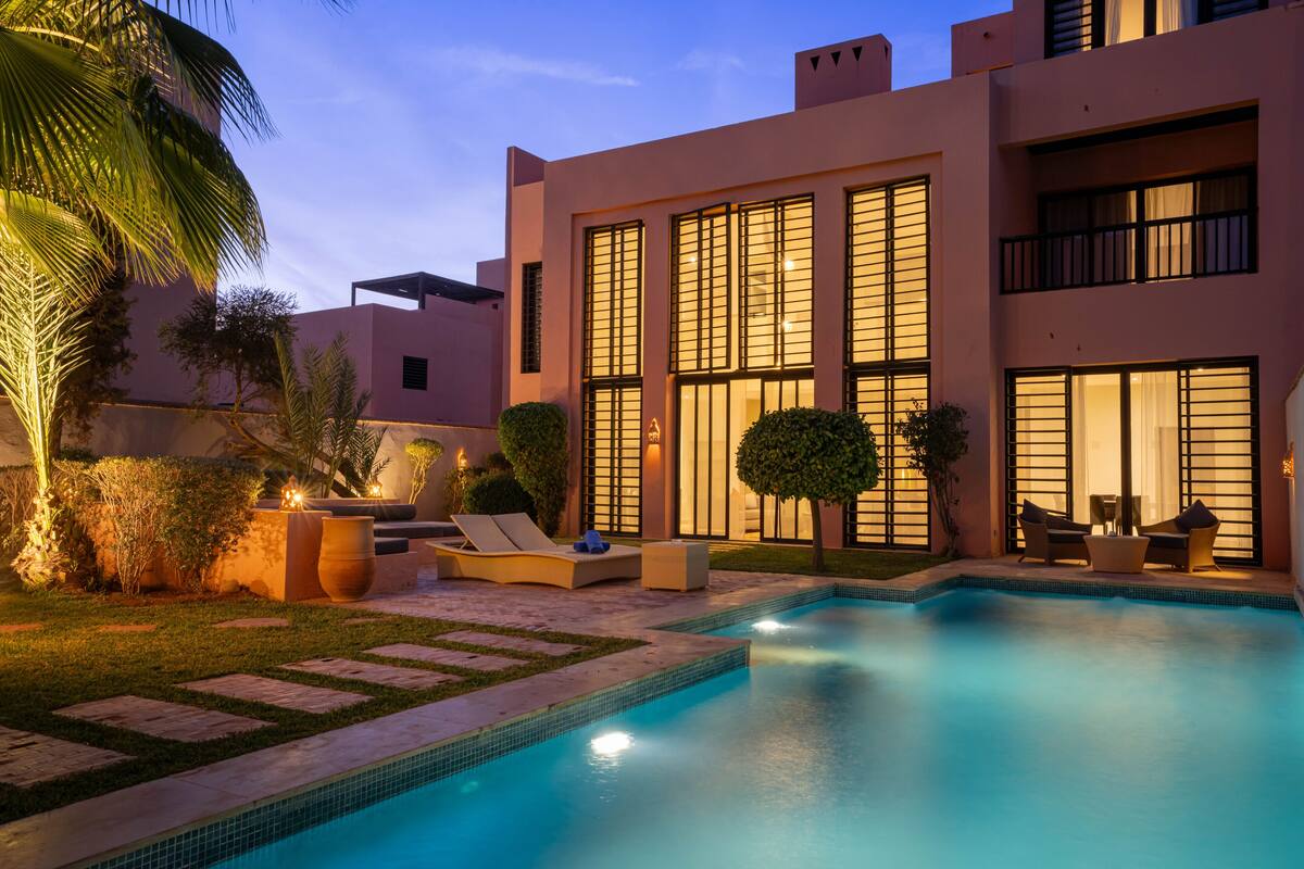 A modern pool area with a clear blue pool, lounge chairs, and a well-maintained garden.