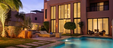 A modern pool area with a clear blue pool, lounge chairs, and a well-maintained garden.