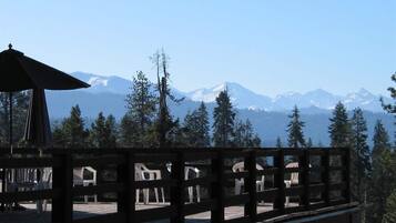 Eine Holzdielen-Terrasse mit Plastikstühlen, mit Blick auf eine gebirgige Landschaft mit schneebedeckten Gipfeln und dichtem Wald.