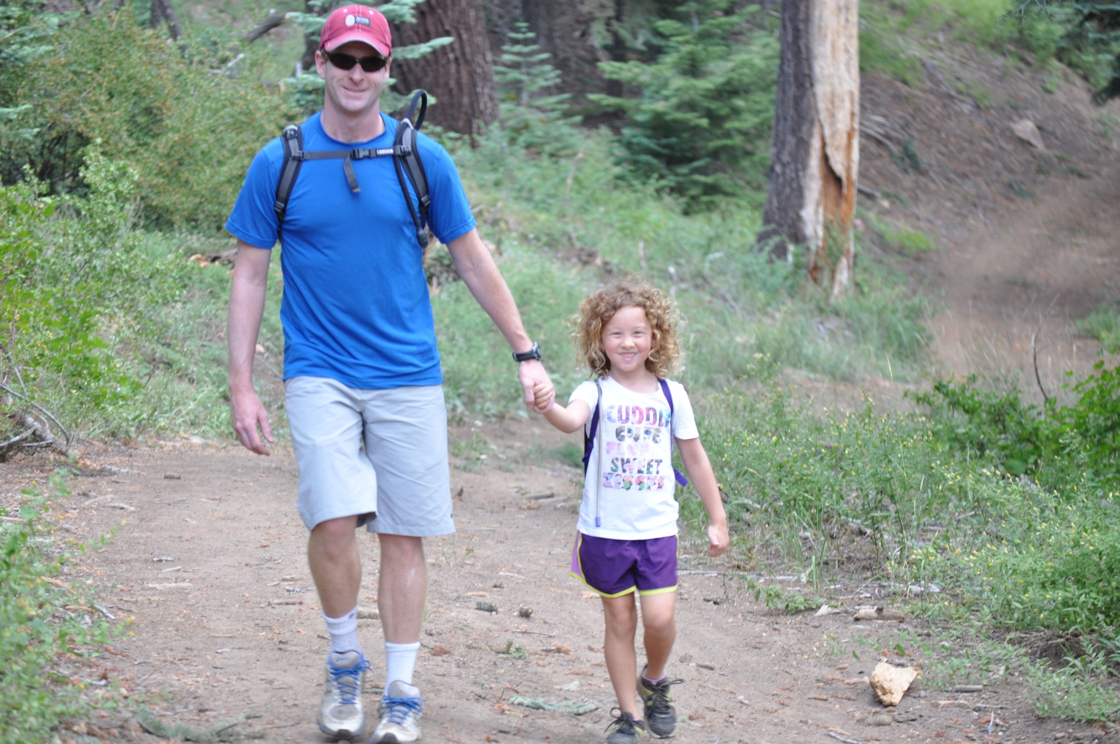 A man and a child walking on a dirt path in a forested area.