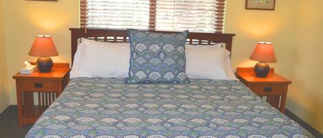 A neatly made bed with patterned bedding, two bedside lamps, and framed pictures on the walls.