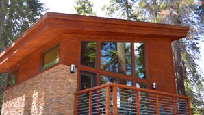 Una cabaña moderna con base de piedra, ventanas amplias y balcón de madera.