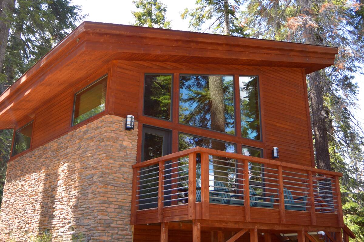 Une cabane moderne avec des fondations en pierre, de grandes fenêtres et un balcon en bois.