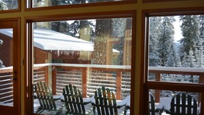 Una terraza de madera con sillones Adirondack cubiertos de nieve y una cabaña de madera al fondo.