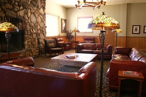 A cozy lounge area with leather sofas, a coffee table, and two floor lamps. A stone wall and a fireplace are visible in the background.