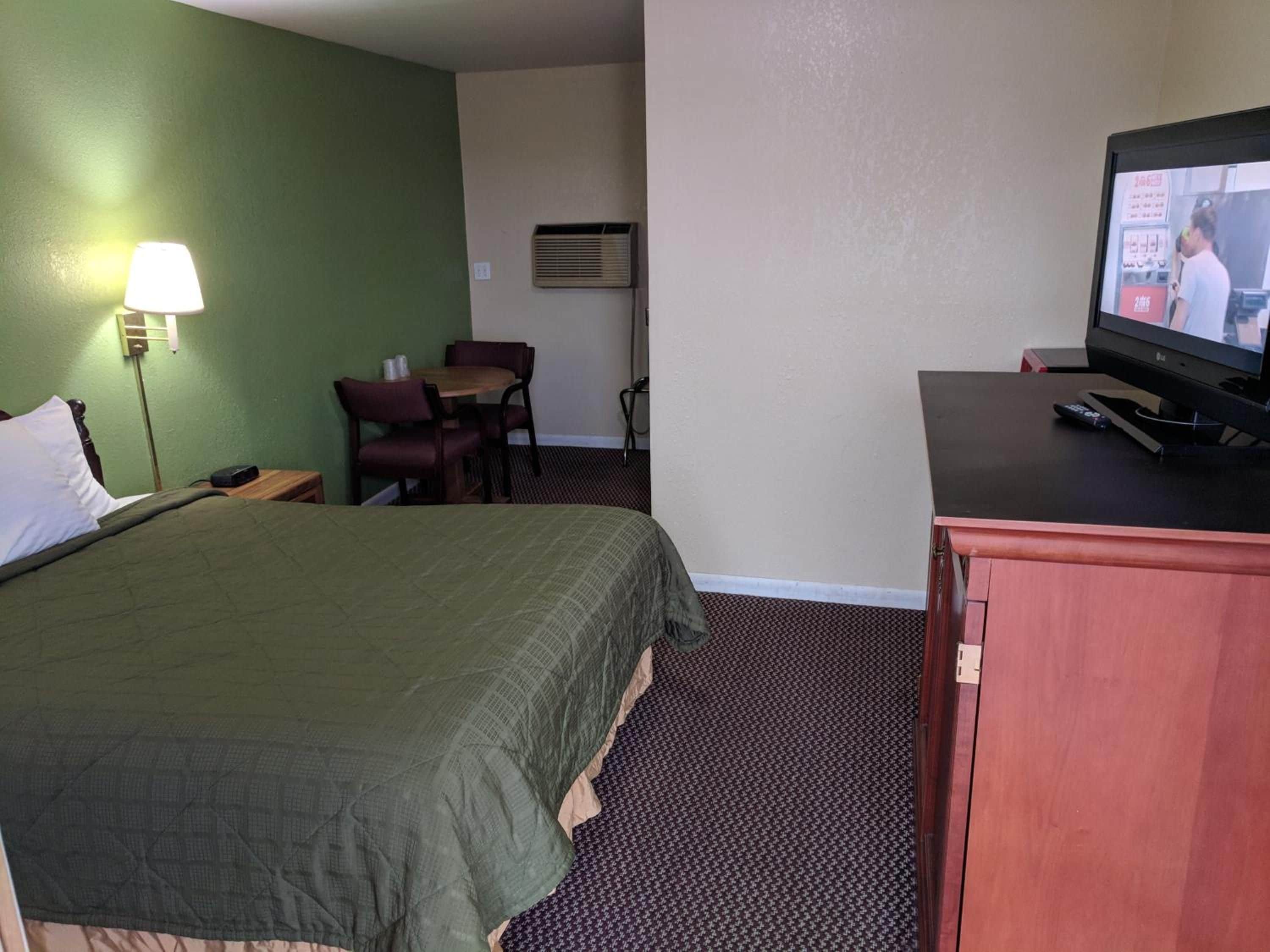 A hotel room with a bed, a desk with a television, a chair, and a lamp.