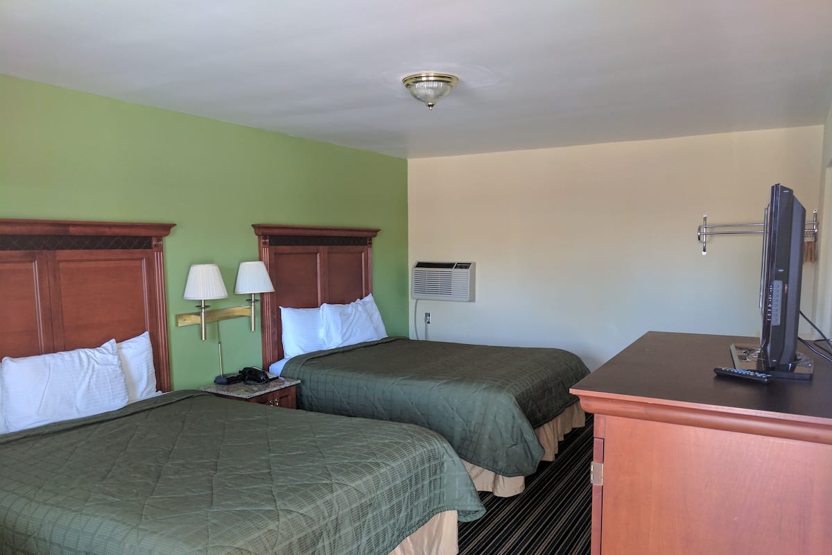 A hotel room with two beds, a desk with a computer, a lamp, and an air conditioning unit.