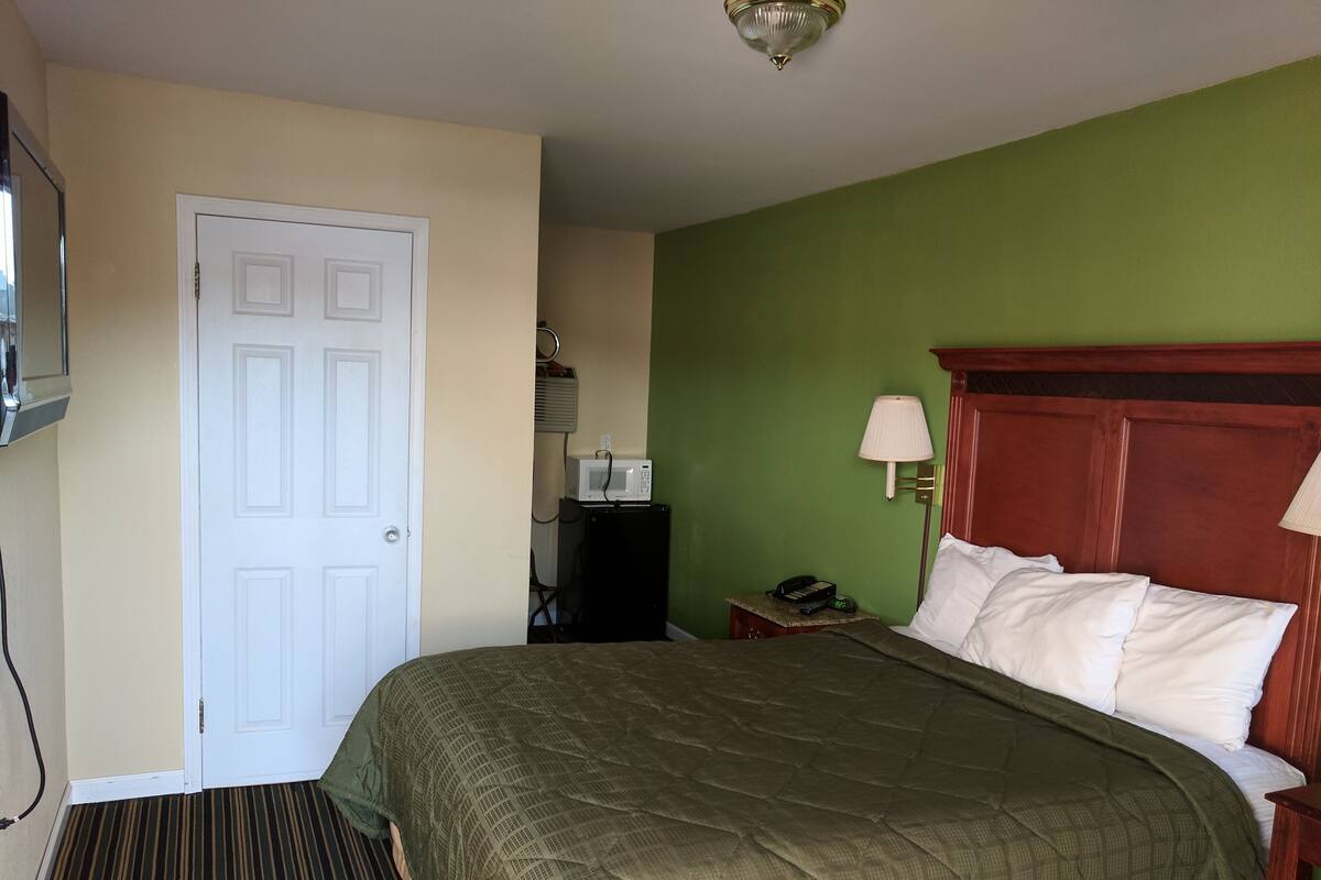 A hotel room with a bed, a door, a microwave, a lamp, and a telephone on a nightstand.