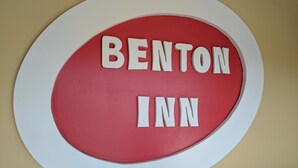 Een rond bord met de woorden “BENTON INN” in witte letters op een rode achtergrond, omgeven door een witte rand.