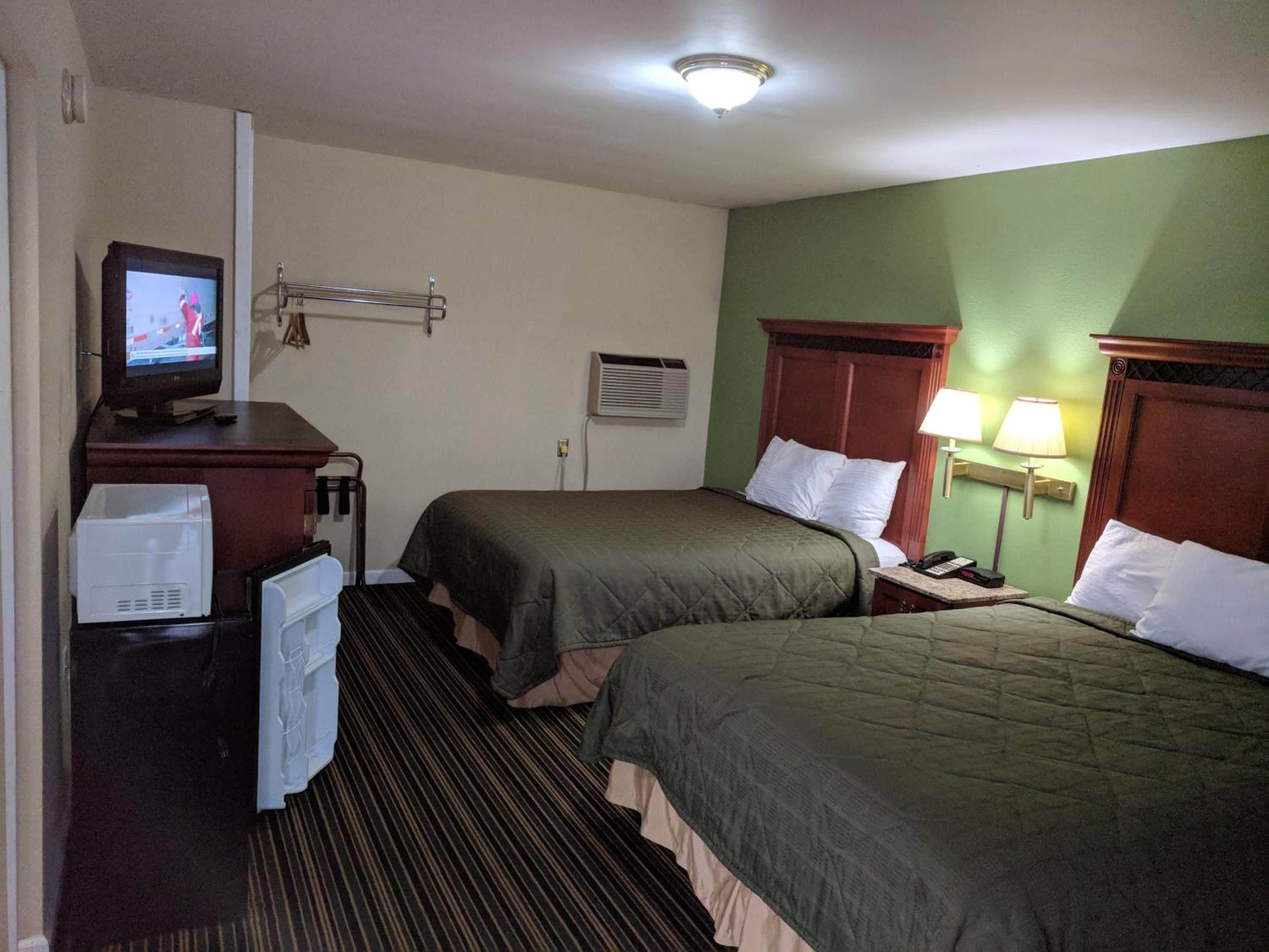 A hotel room with two beds, a television, a desk with a computer, and a lamp.