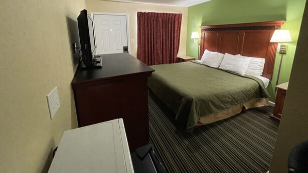 Een hotelkamer met een bed, een bureau, een televisie, een lamp en een raam met gordijnen.