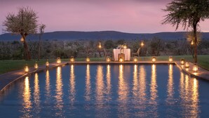 Ein Pool mit Tisch und Stühlen, umgeben von Bäumen und Blick auf den Sonnenuntergang.
