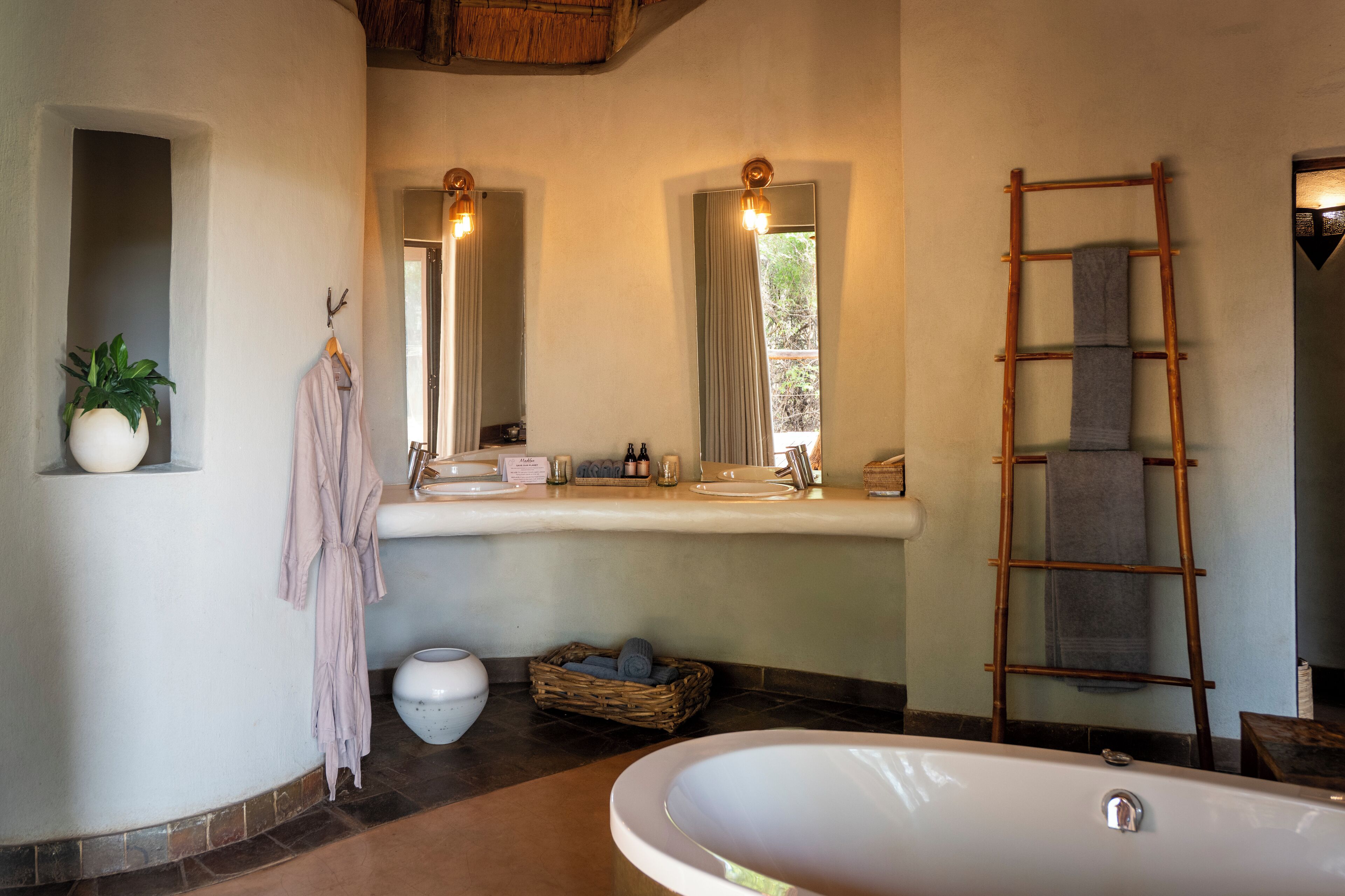 A bathroom with a bathtub, a large mirror, a wooden ladder, a potted plant, and a wicker basket.