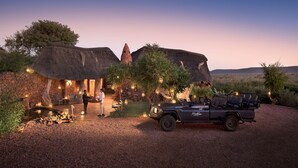 Eine Safari-Lodge mit einem strohgedeckten Gebäude, einem Fahrzeug und einer Schotterzufahrt.