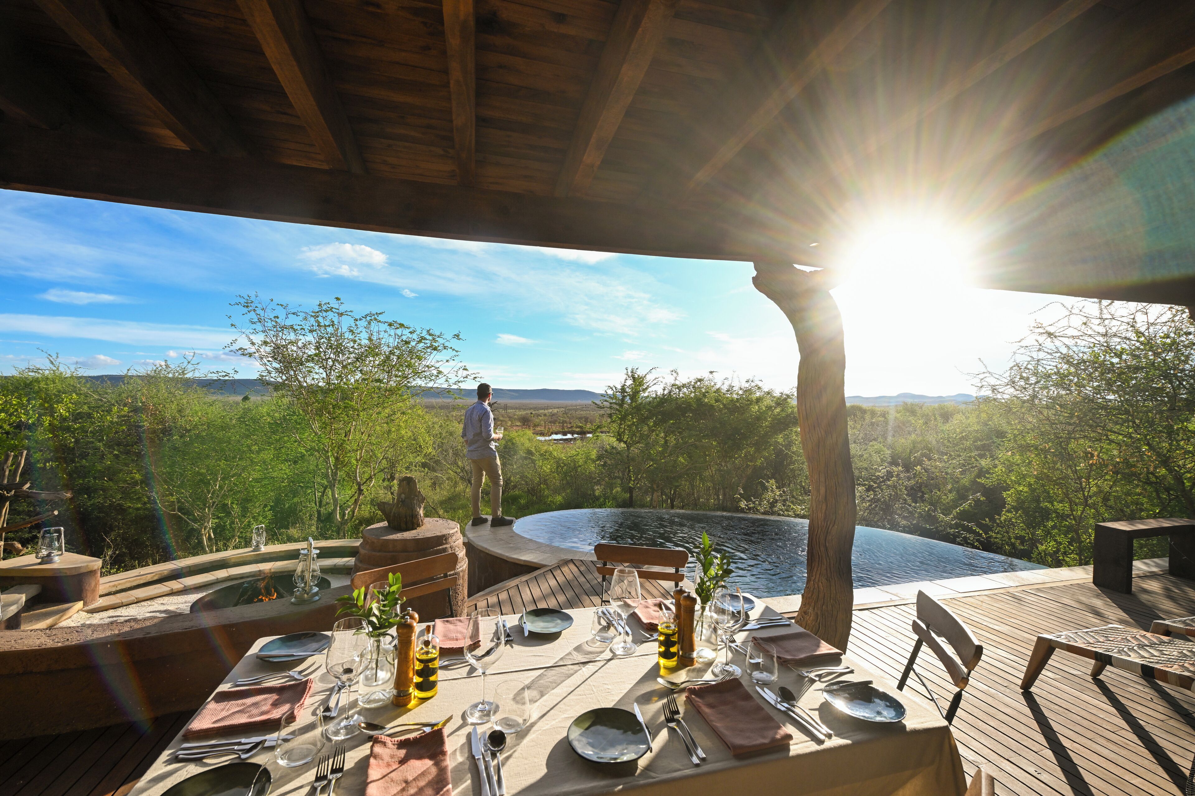 An outdoor dining area with a table set for two, overlooking a body of water and a mountainous landscape.