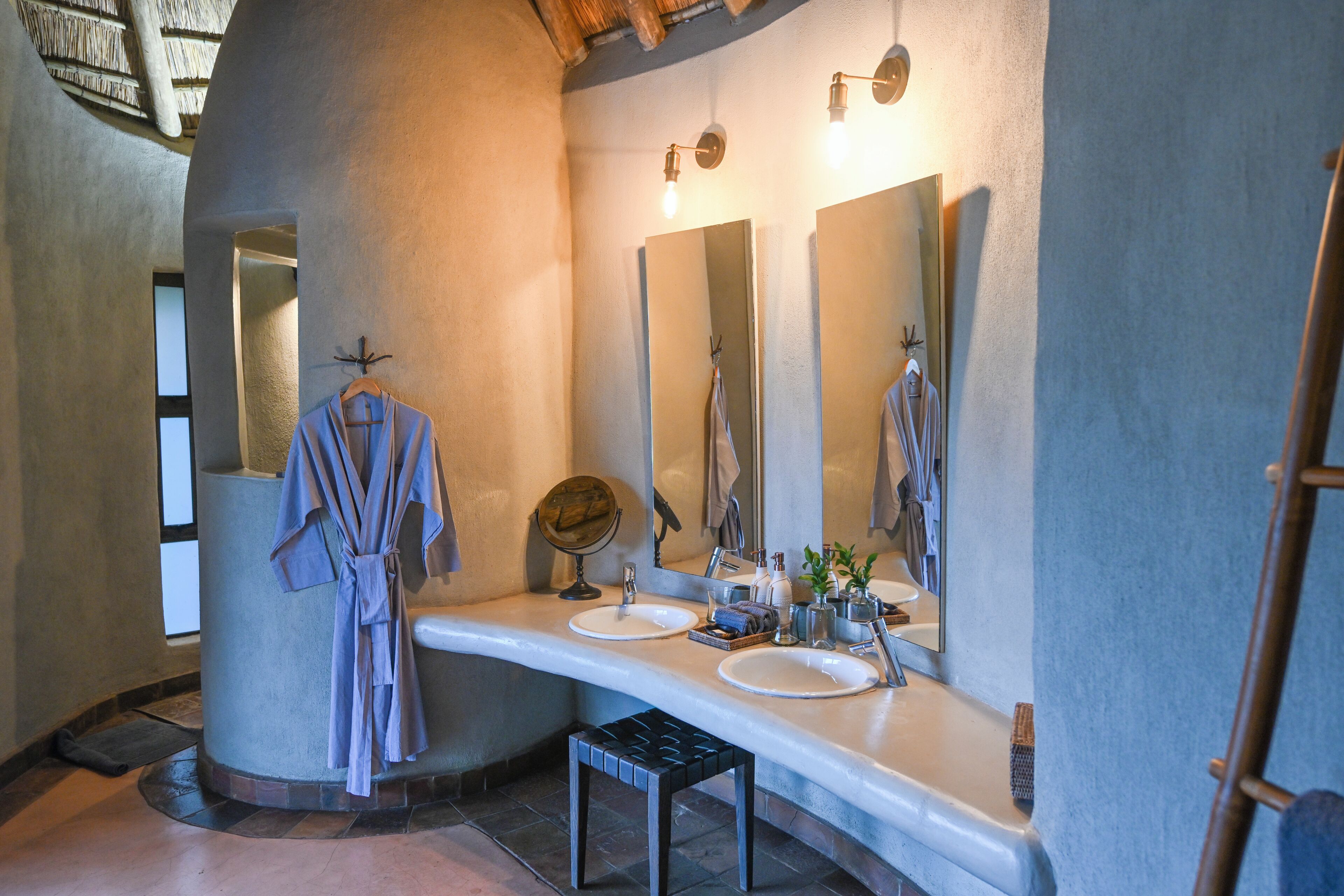 A modern bathroom with a curved vanity, two sinks, a large mirror, and a robe hanging on the wall.
