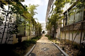 A narrow pathway flanked by bamboo plants and a patterned stone floor leading to a building entrance. - Garden Hotel (Suzhou)