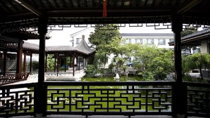 A traditional Chinese pavilion with a tiled roof, a decorative railing, and a view of a courtyard with a pond and greenery. - Garden Hotel (Suzhou)