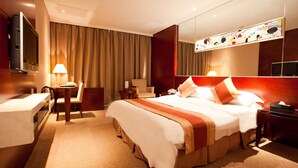 A hotel room with a large bed, a desk, a chair, a TV, and a mirror. - Garden Hotel (Suzhou)