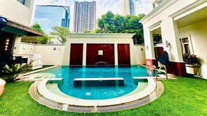 Una piscina de diseño circular, rodeada por un césped cuidado y un edificio con un cartel que dice "Asoke Residence".