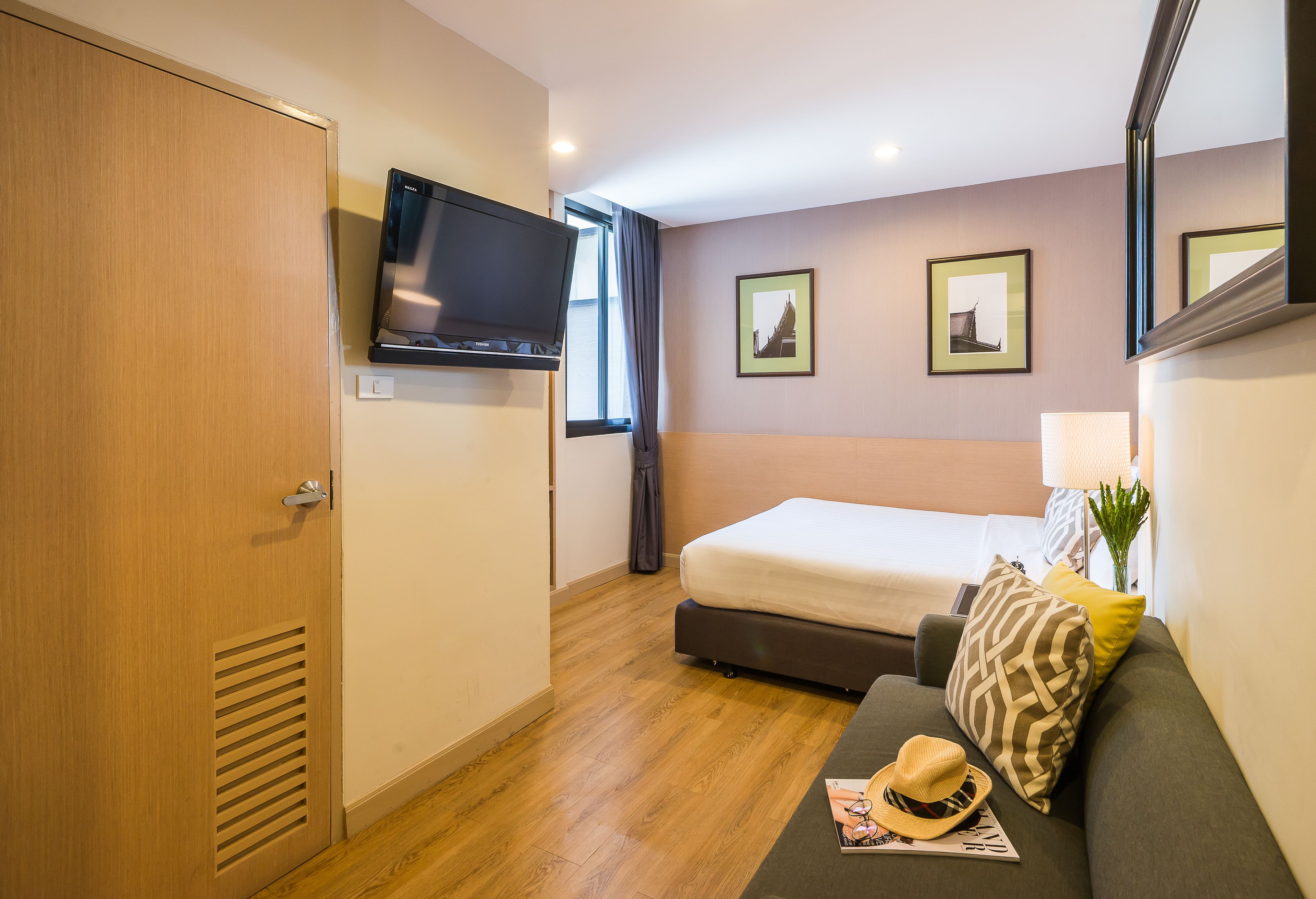 A hotel room with a bed, a television, a window with curtains, and a wall-mounted picture.