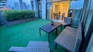 Un patio exterior moderno con puerta de vidrio que da a un área de comedor, con vistas a la ciudad.