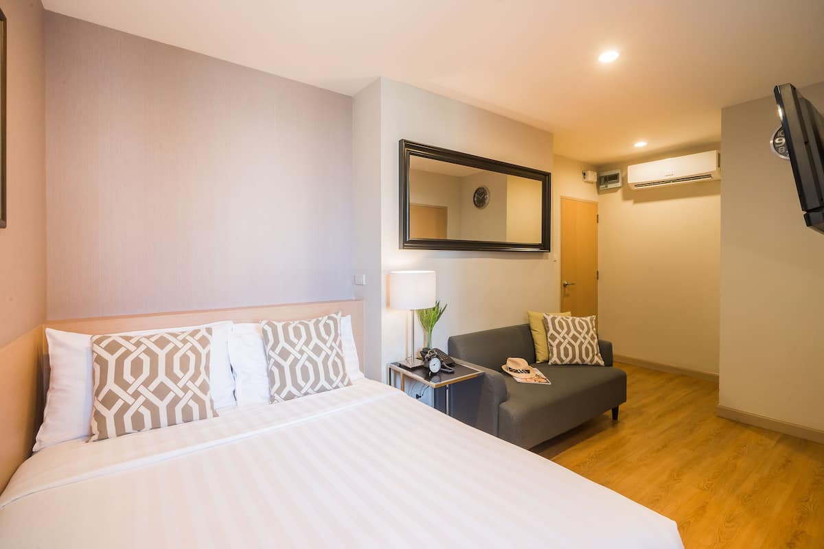 Une chambre d’hôtel comprenant un lit, un canapé, une petite table avec une lampe, un miroir et un appareil de climatisation.