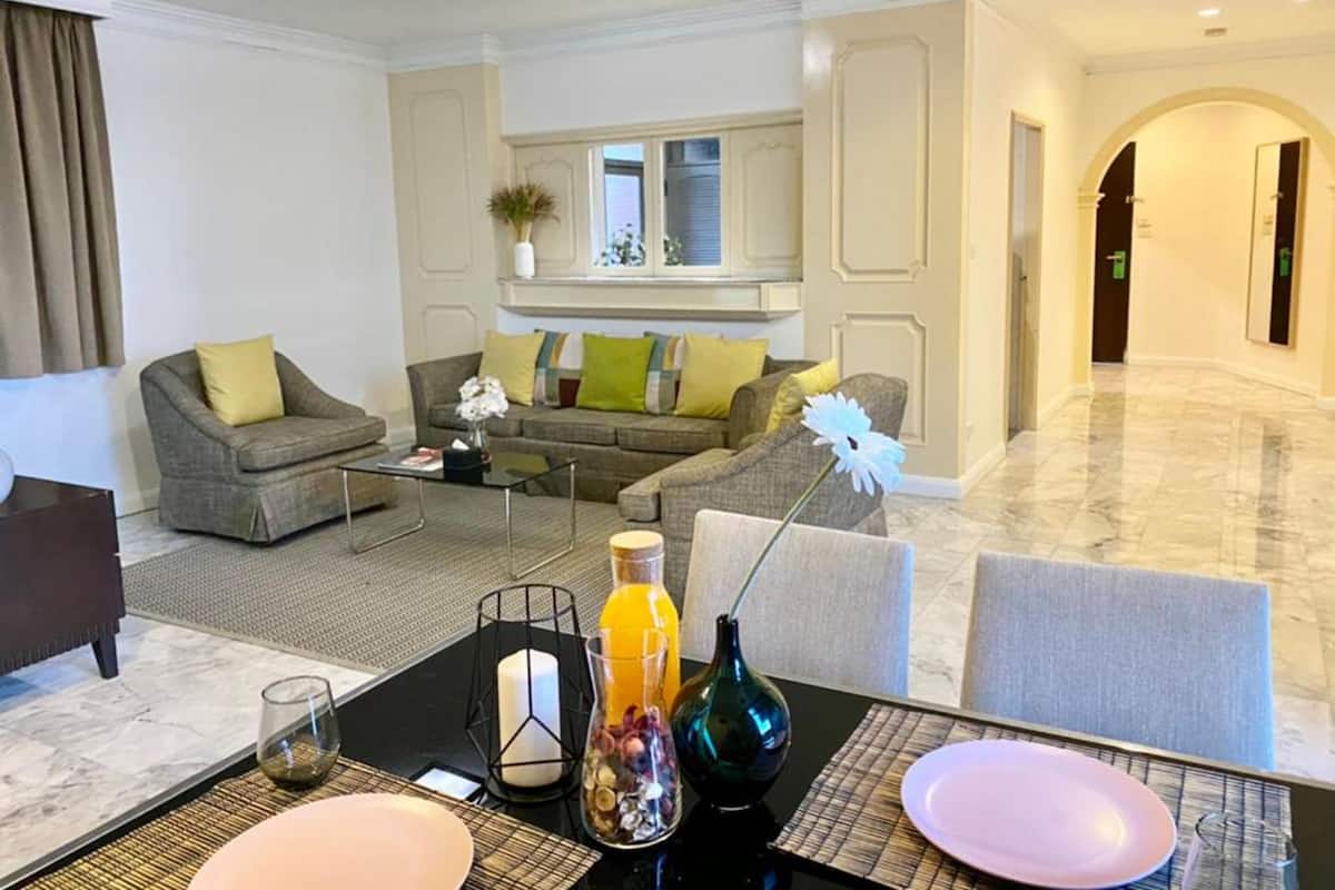 Un salon moderne comprenant un ensemble de canapés, une table basse et un coin repas avec une table dressée pour deux personnes.