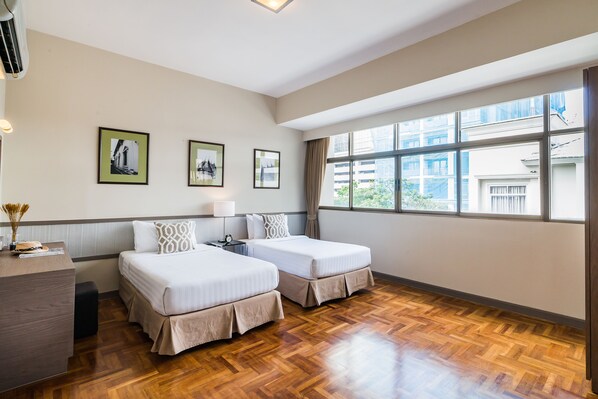 A hotel room with two beds, a desk, and a large window.