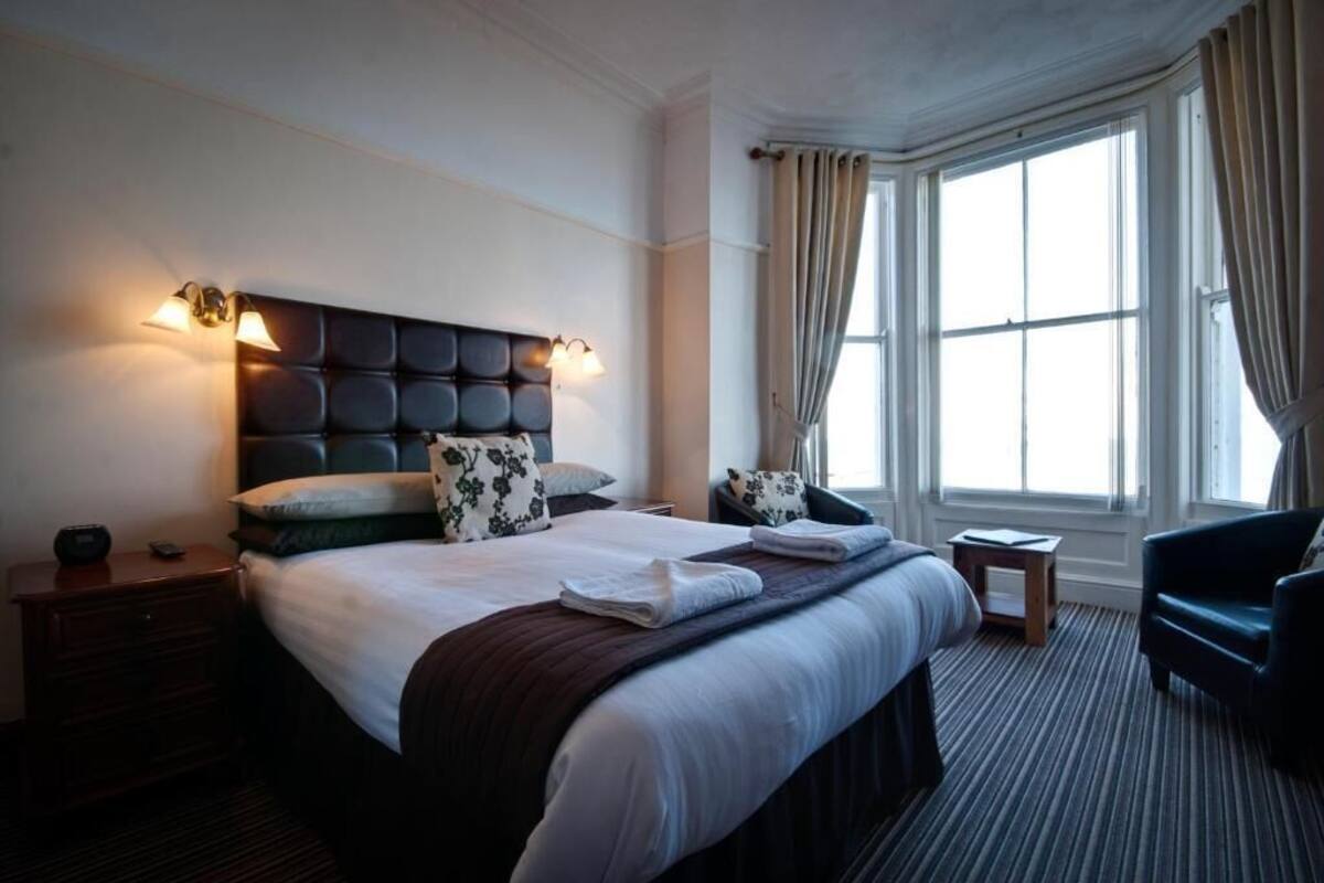 A hotel room with a large bed, two bedside tables, a nightstand, a chair, and a window with curtains.