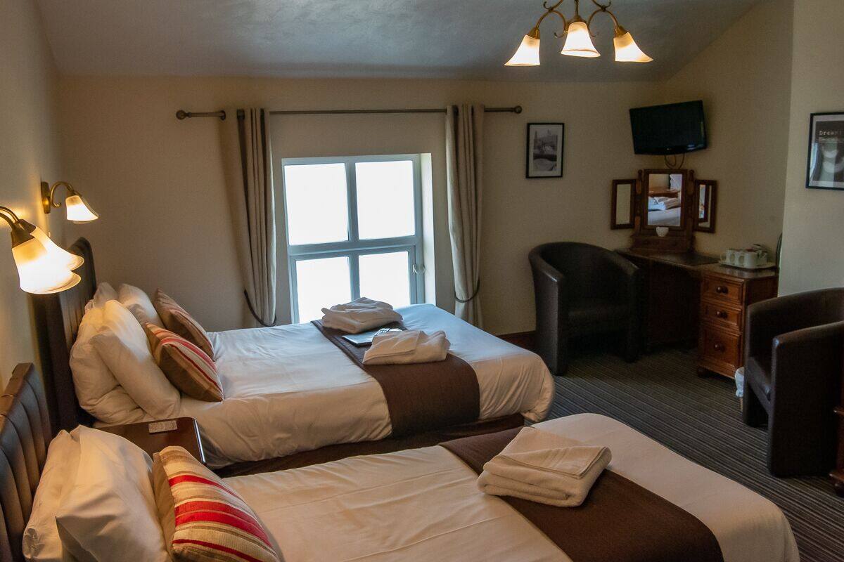 A hotel room with two beds, a desk with a chair, a television, and a window with curtains.