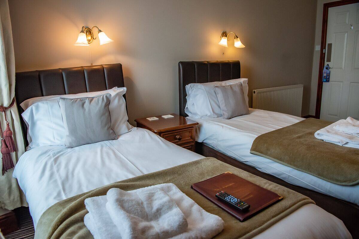 A hotel room with two beds, each with a headboard, bedside tables, and lamps.