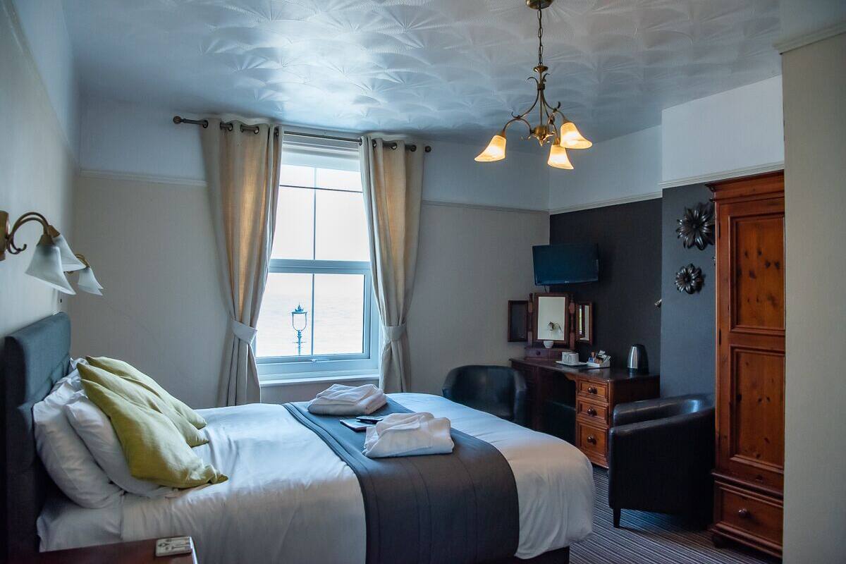A hotel room with a bed, a desk, a chair, a wardrobe, and a television.