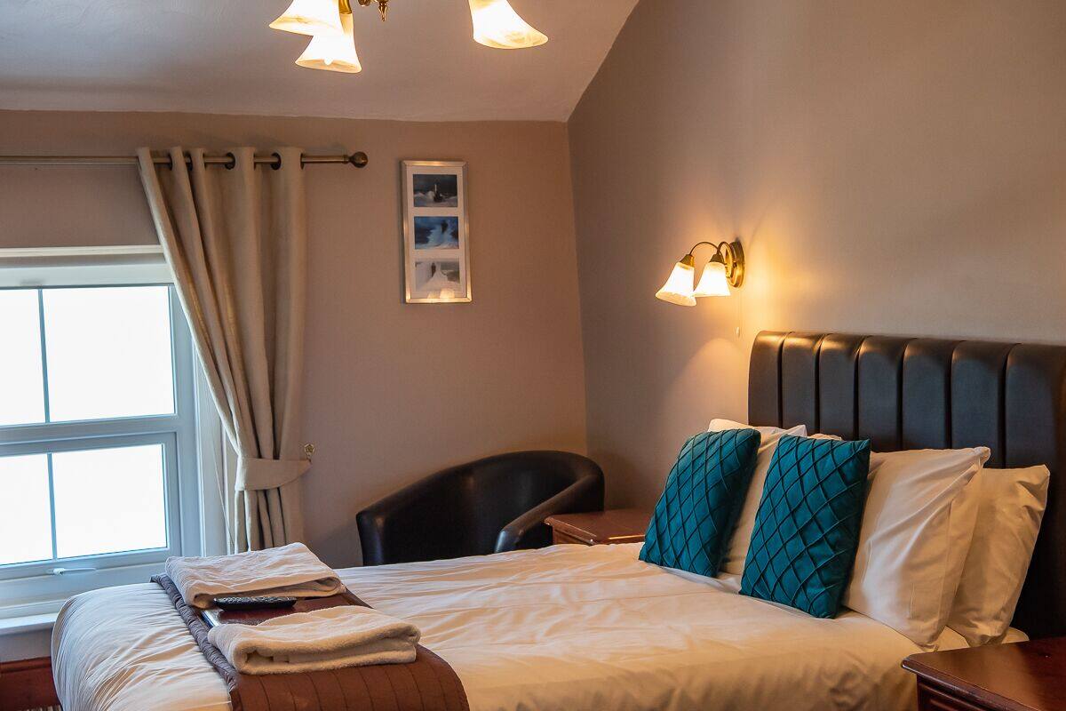 A hotel room with a bed, a chair, a bedside table, and a window with curtains.