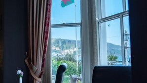 Een eetruimte met een tafel gedekt voor twee personen, een vlag buiten het raam en uitzicht op een kustlandschap.