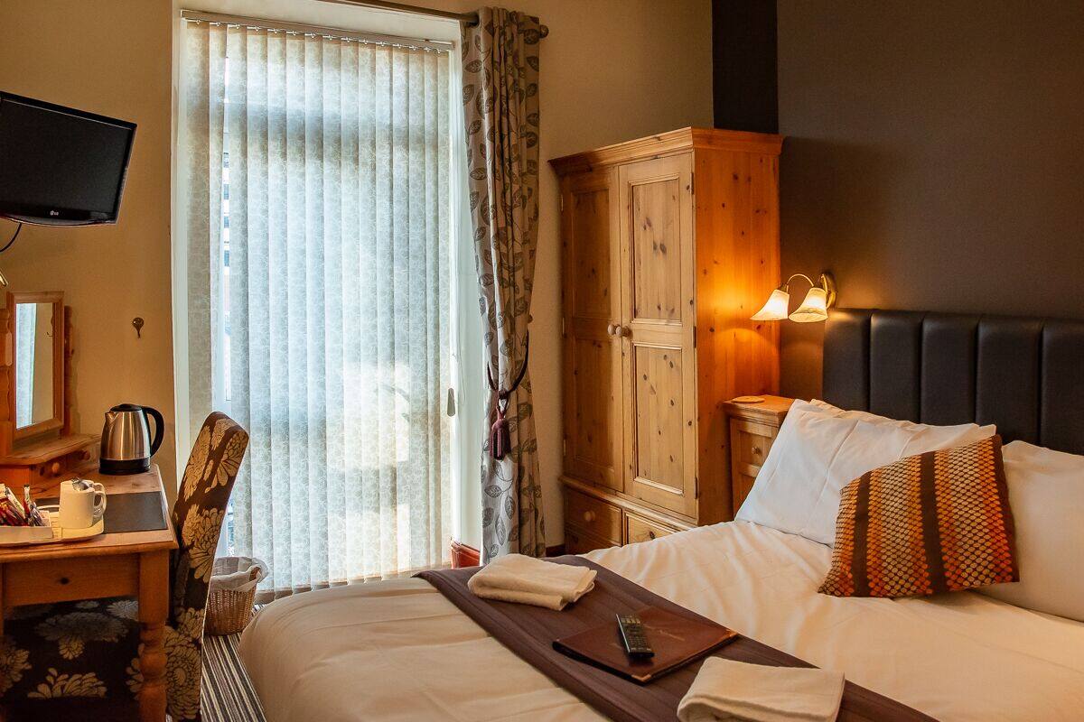 A hotel room with a bed, a desk with a kettle, a television, and a wardrobe.