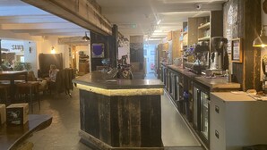 Uma área de bar com balcão de madeira, assentos e um extintor visível.