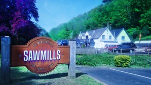 Placa para Sawmills Eat Drink Store, com design rústico, rodeada por vegetação e uma estrada.