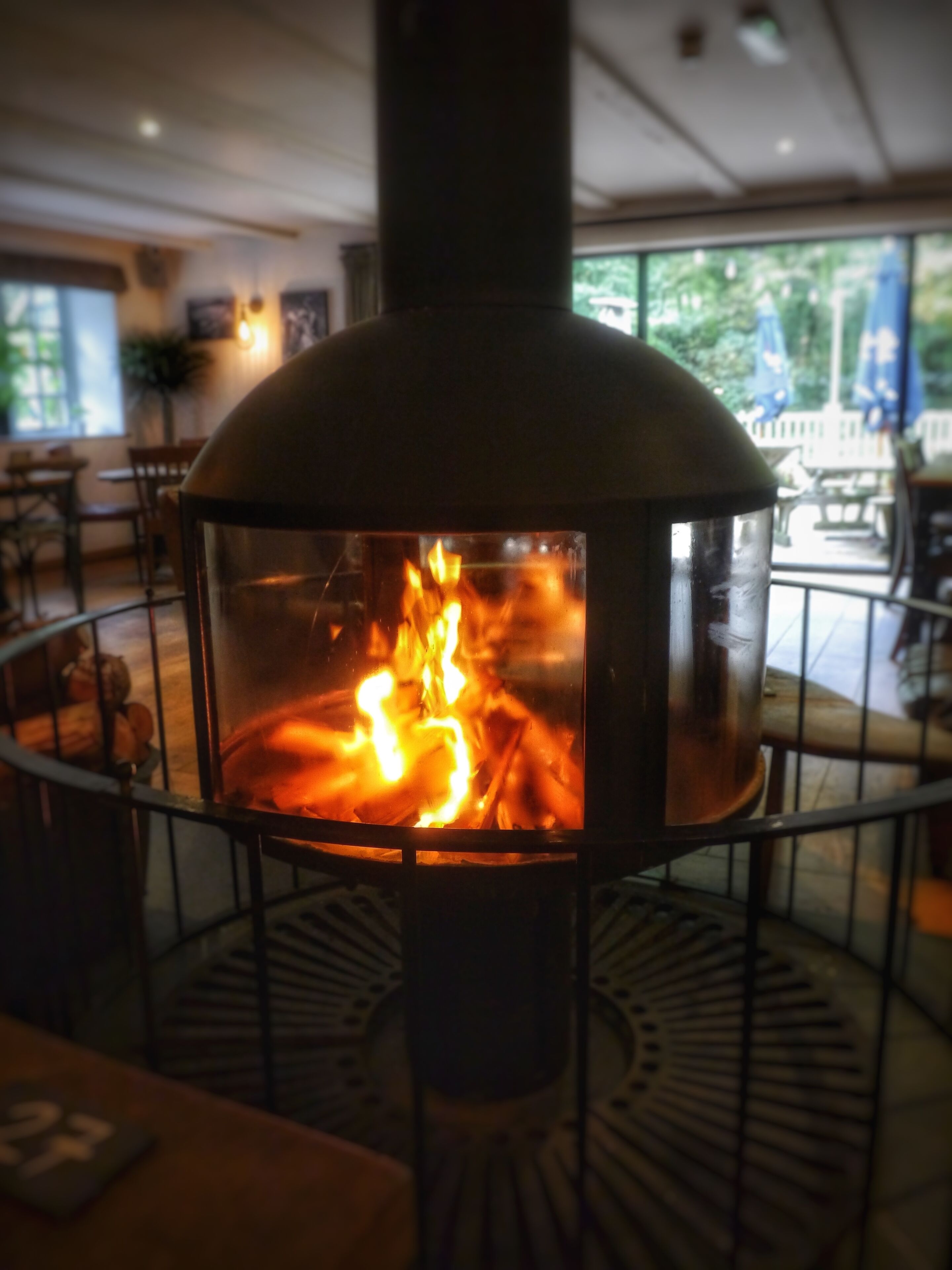 En vedeldad kamin i ett runt rum med ett metallräcke och ett bord i förgrunden.