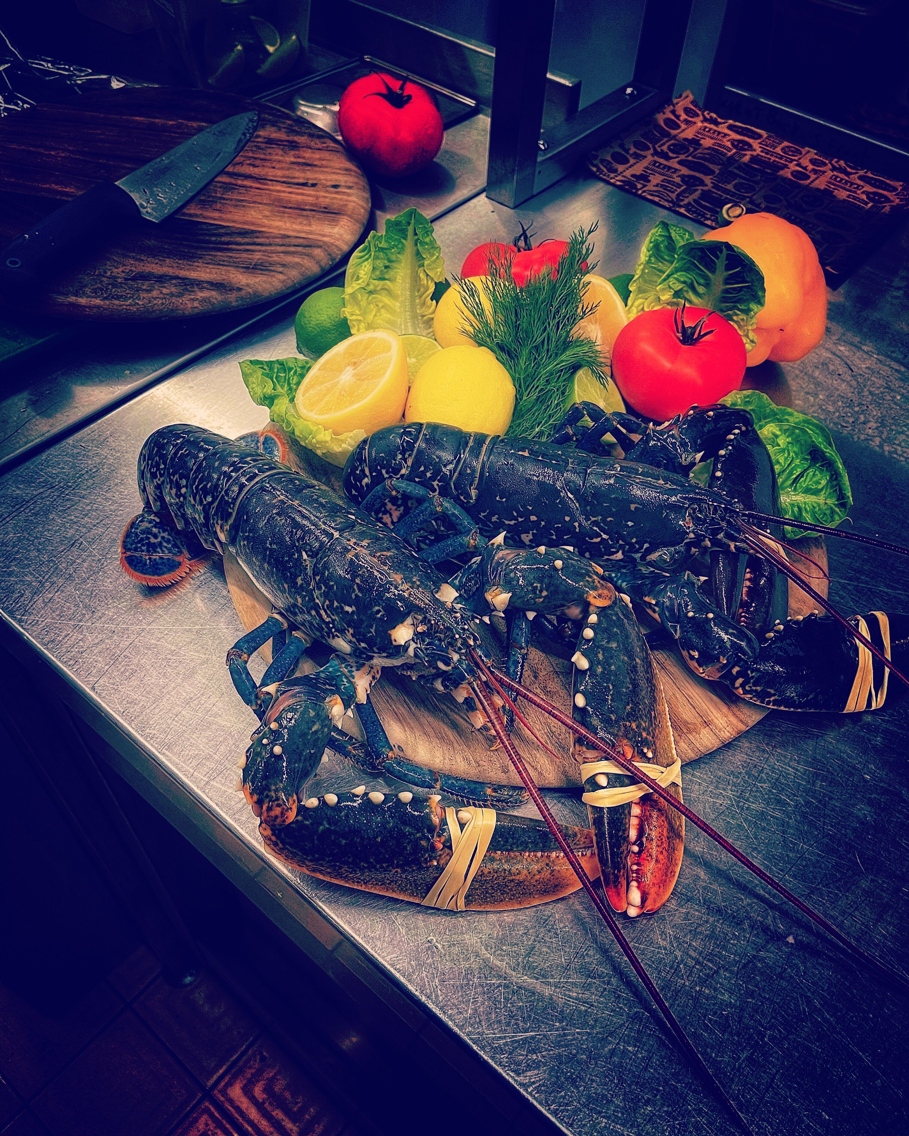 A lobster on a wooden cutting board with lemons, tomatoes, and lettuce.