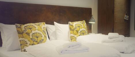 A neatly made bed with white linens and yellow patterned pillows, a wooden headboard, and a painting on the wall.