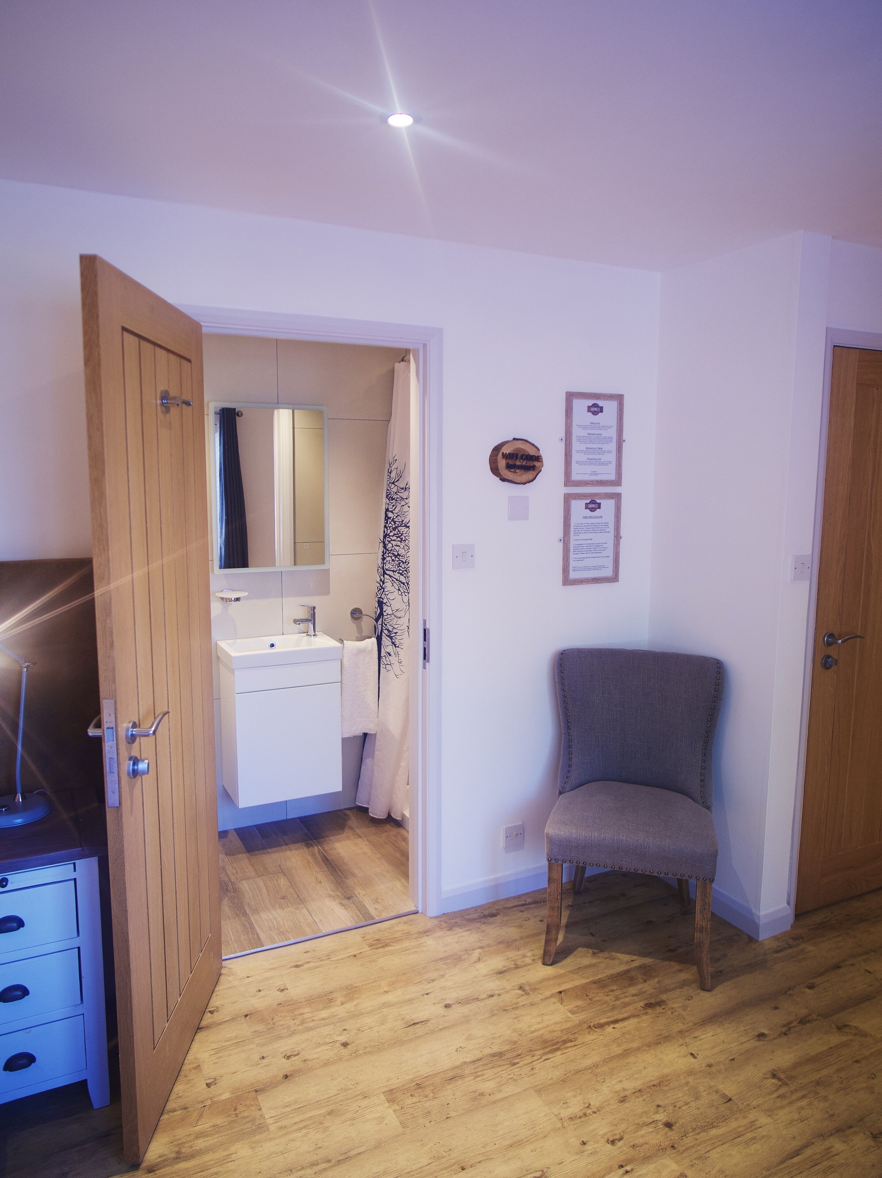 A room with a wooden floor, a white sink, a mirror, a towel, a chair, and a door.