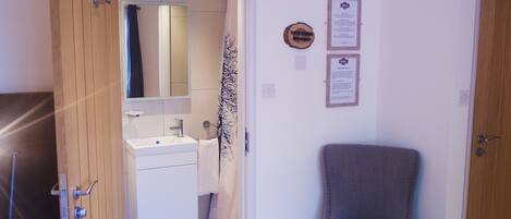 A room with a wooden floor, a white sink, a mirror, a towel, a chair, and a door.