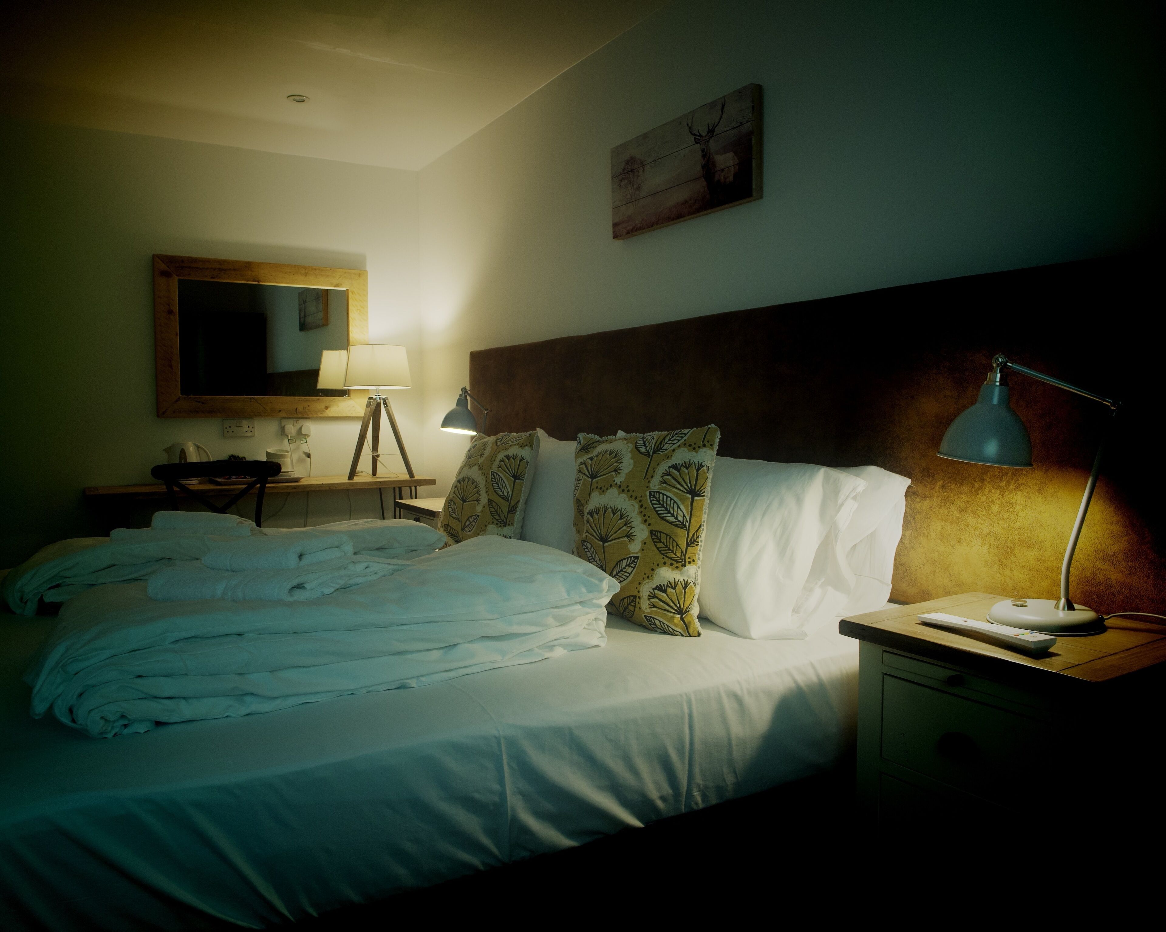 A hotel room with a bed, bedside lamps, a desk with a lamp, a chair, and a wall-mounted mirror.