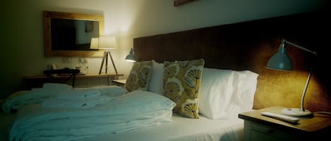 A hotel room with a bed, bedside lamps, a desk with a lamp, a chair, and a wall-mounted mirror.